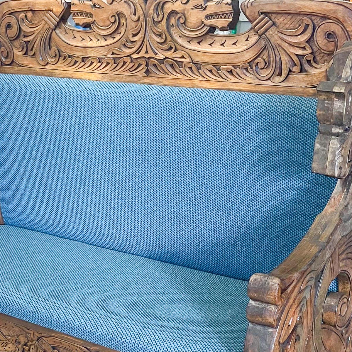 Nærbilde av historisk sittebenk i tre med blått stoff