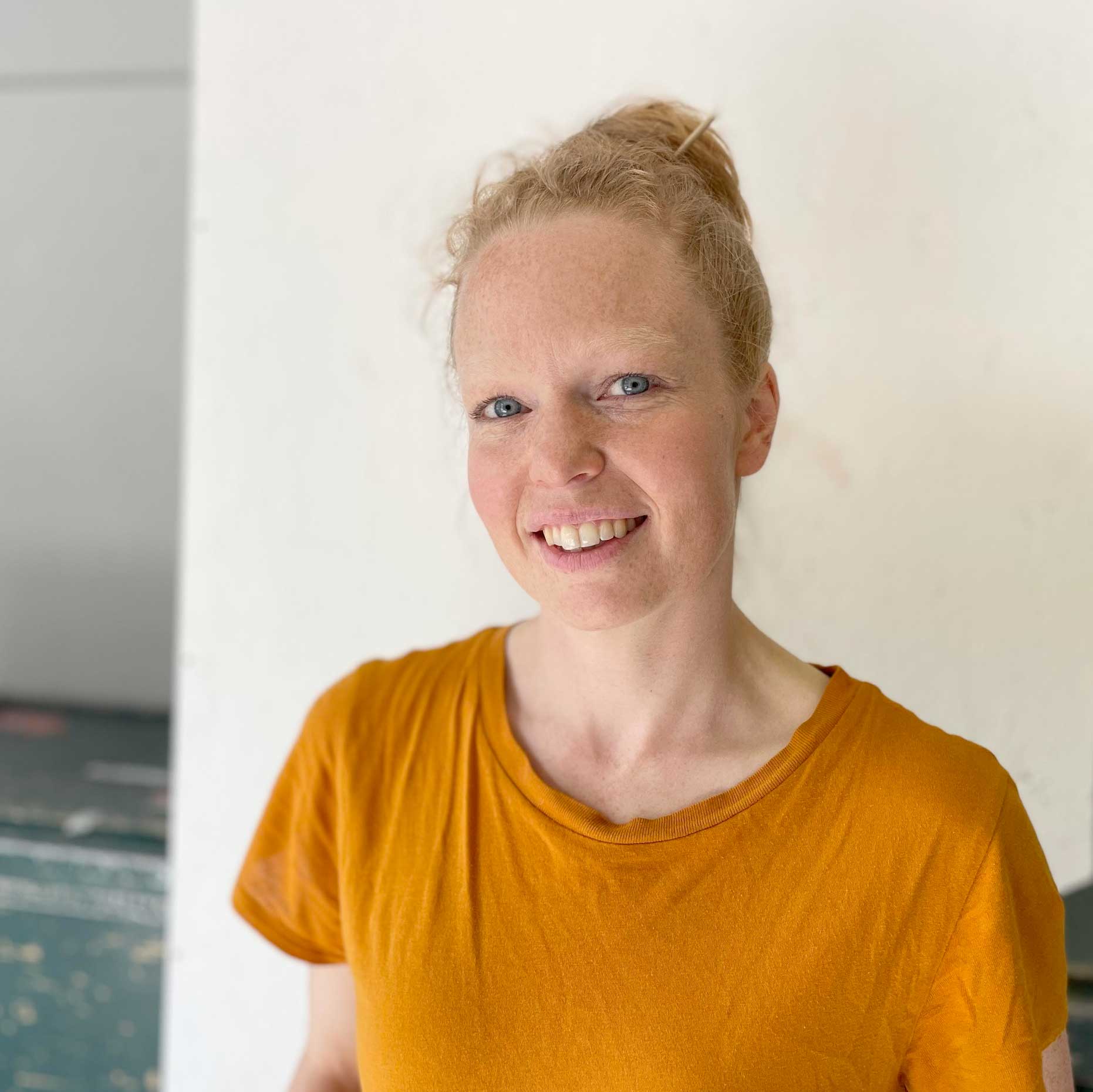 Rødhåret kvinne i oransjefarget t-skjorte som smiler i kameraet.